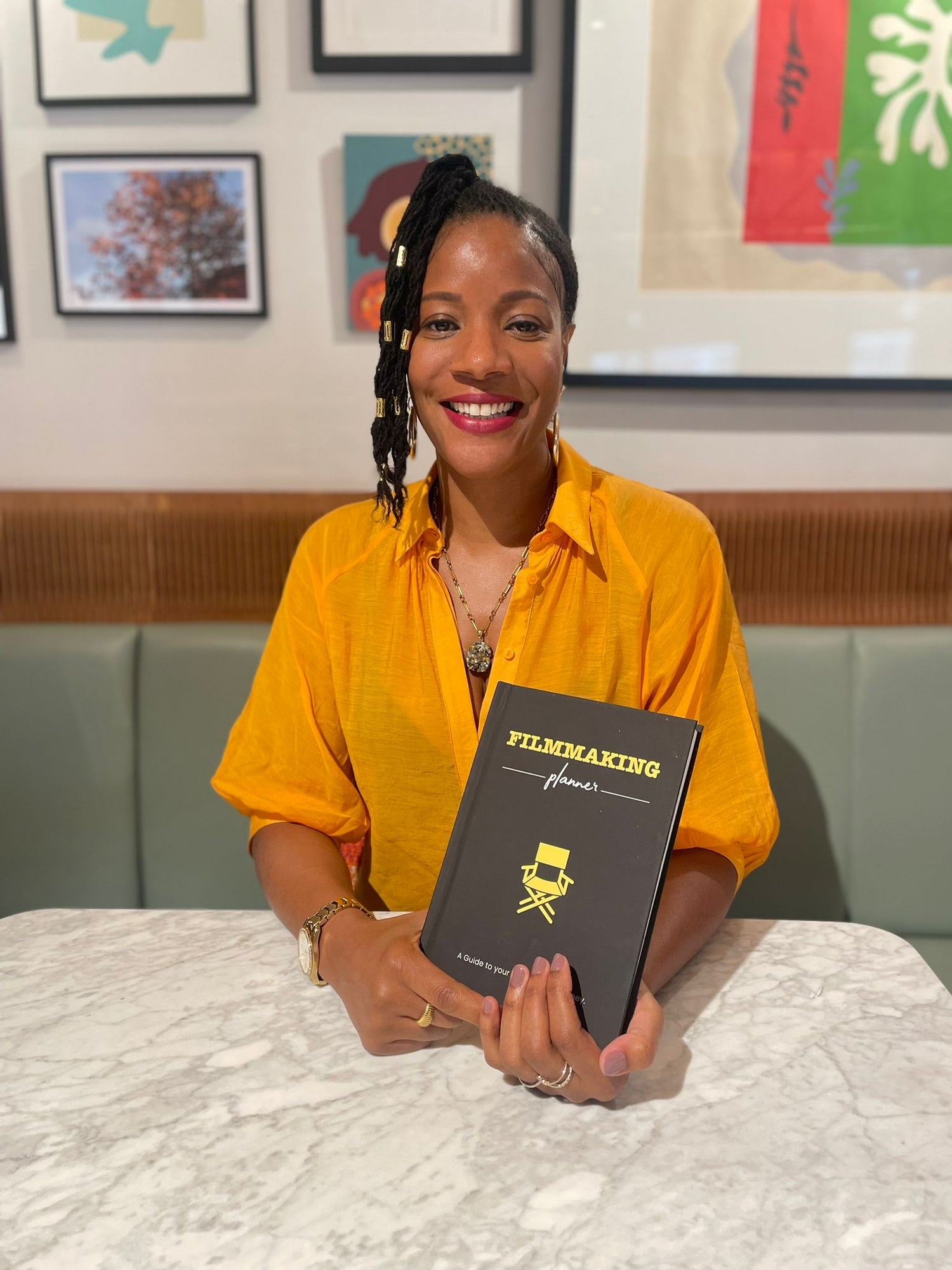 A photo of the filmmaking planner's founder, aysha scott, holding a planner in her hands, sat down at a restaurant