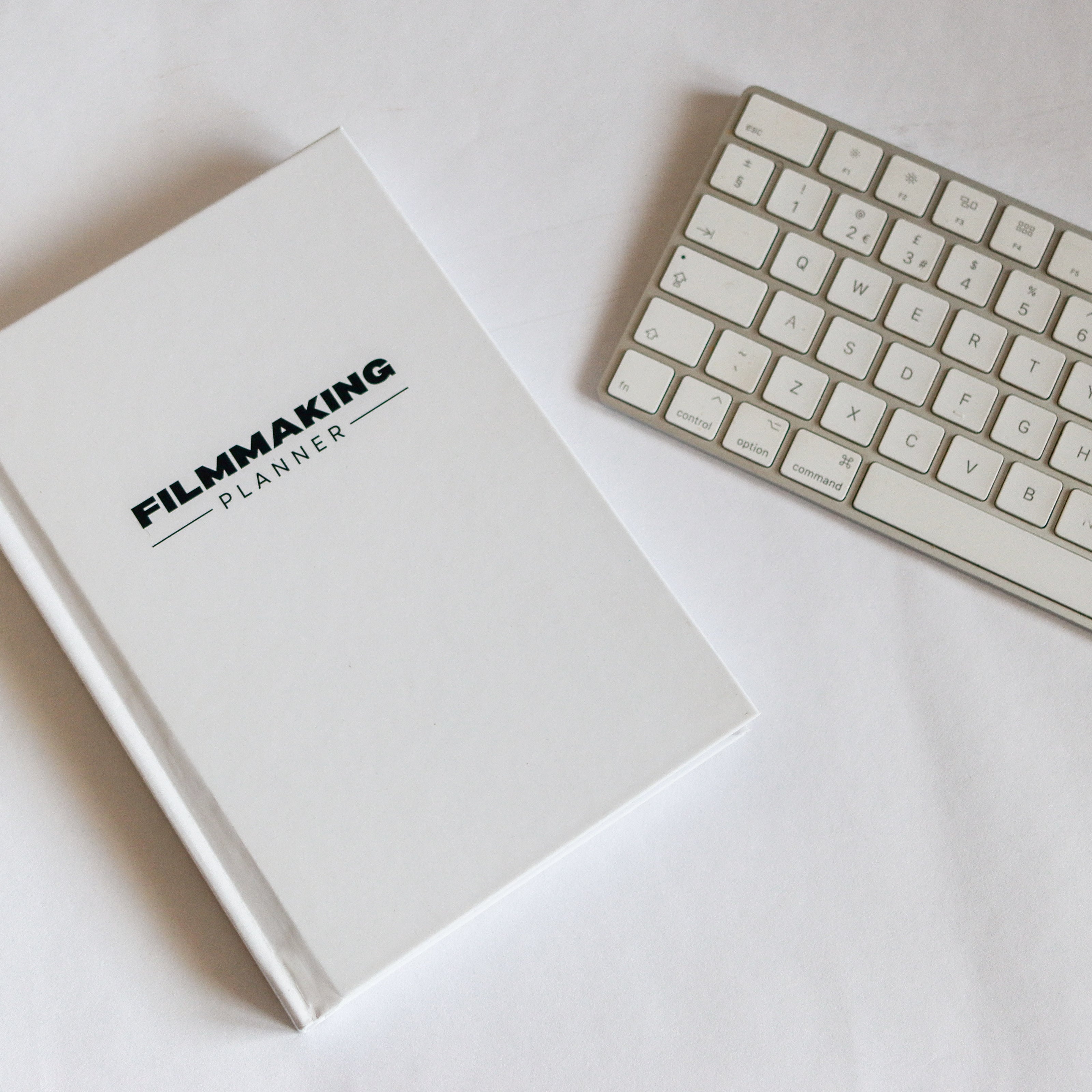 A5, Hardback white book laid flat with Filmmaking Planner across the front next to an Apple Mac keyboard. 