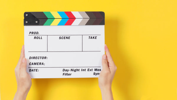 hands holding a clapperboard behind a bright yellow backdrop for film editing. Filmmaking Planner 