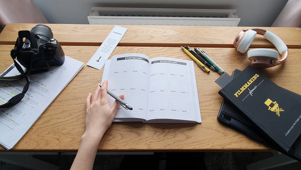 Filmmaking Planner on Storyboard Page with Filmmaking Planner, headphones and camera on desk. 