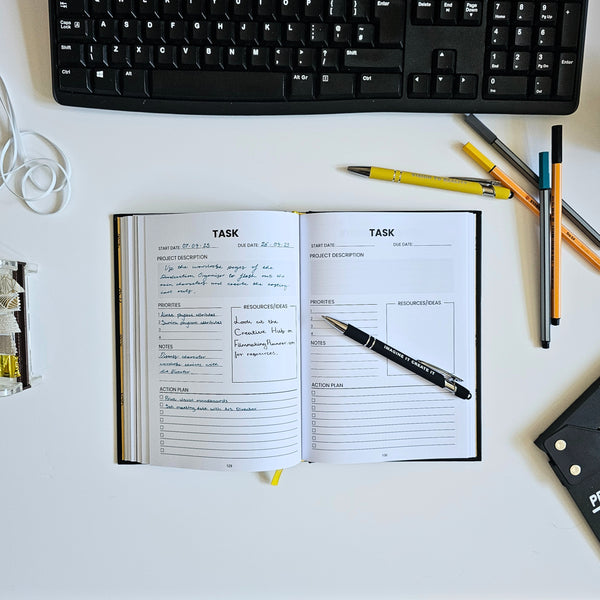 Open planner with task listings on a desk with a keyboard and pens.