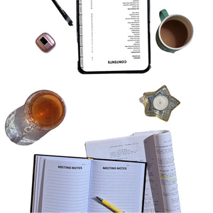 Flat lay of a notebook with 'Meeting Notes' pages, a tablet, a mug, and a candle on a white background.