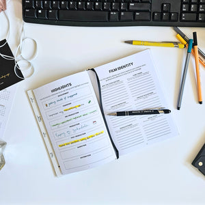 Notebook with film identity planning on a desk with pens and a keyboard.