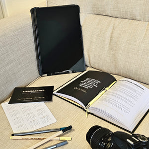 Open notebook with checklist on a couch next to a camera and pens