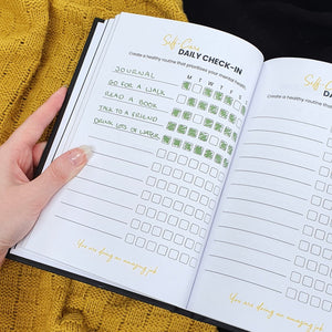 Filmmaking Planner open on filled in self-care page, with a hand holding the book. 