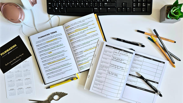 Open notebook with planning pages on a desk with pens and a keyboard.